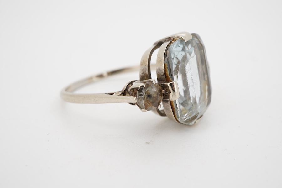 A mid 20th century white metal and single stone cushion cut blue topaz set dress ring, with two stone topaz set shoulders, size R.